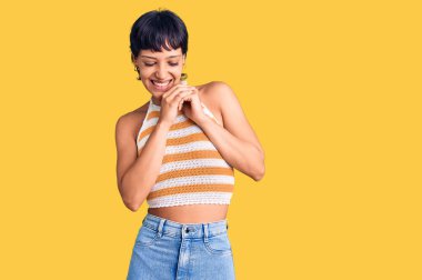 Kısa saçlı genç esmer kadın günlük kıyafetler giyiyor. Gergin ve heyecanlı bir şekilde çenesine bakıp yan tarafa bakıyor. 