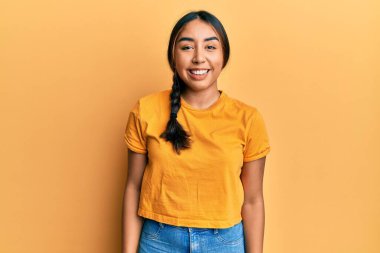 Gündelik kıyafetler giyen, yüzünde gülümsemeyle yan yana bakan genç Latin kadın, doğal bir ifade. Kendinden emin gülen. 