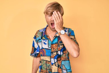 Young blond man wearing summer shirt yawning tired covering half face, eye and mouth with hand. face hurts in pain. 