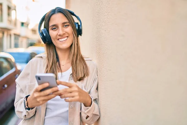 若い白人女性は 市内でスマートフォンやヘッドフォンを使用して幸せな笑顔 — ストック写真
