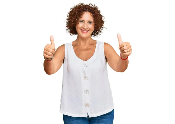 手で積極的なジェスチャーを行うことを承認カジュアルな白いシャツを着て美しい中年の成熟した女性 親指アップ笑顔と成功のために幸せ 勝者のジェスチャー — ストック写真
