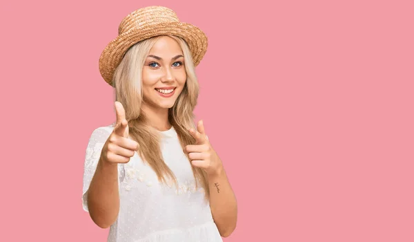 若いブロンドの女の子は 幸せと面白い顔でカメラに指を指して夏の帽子をかぶっています 良いエネルギーと振動は — ストック写真