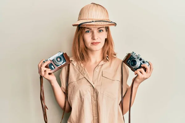 Young caucasian woman wearing explorer hat and vintage camera relaxed with serious expression on face. simple and natural looking at the camera.