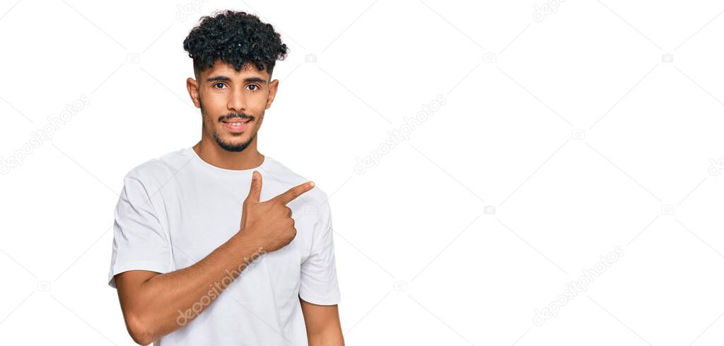 Young arab man wearing casual white t shirt cheerful with a smile on face pointing with hand and finger up to the side with happy and natural expression 