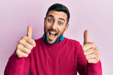 Latin asıllı genç adam gündelik giysiler giyip olumlu jestler yapıyor. Elleriyle gülümsüyor ve başarı için seviniyor. kazanan jest. 