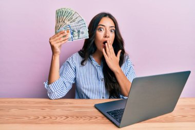 Ofiste çalışan güzel esmer genç bir kadın, elinde dolarlarla ağzı kapalı, şok olmuş ve hata yapmaktan korkan bir kadın. şaşırmış ifade 