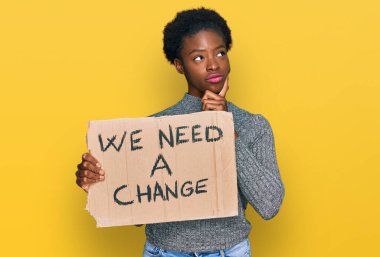Genç Afro-Amerikan kızı elinde bir değişiklik pankartı tutarken ciddi bir yüze ihtiyacımız var soru sorarken çene ve kafa karıştırıcı bir fikir hakkında düşünceli. 