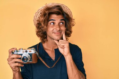 Şapka takan İspanyol genç adam elinde eski bir kamerayla ciddi bir yüzle eli çenesinde soru soran, kafa karıştırıcı bir fikir hakkında düşünceli. 