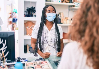 Giyim mağazasında çalışan, tıbbi maske takan Afro-Amerikan bir kadın.