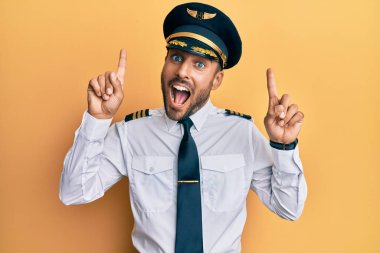 Yakışıklı İspanyol pilot üniforması giyiyor. Şaşırmış, şaşırmış, parmaklarıyla işaret ediyor ve kollarını kaldırıyor.. 