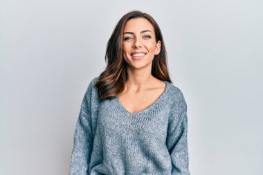 Genç esmer kadın sıradan bir kazak giyiyor ve yüzünde mutlu ve havalı bir gülümseme var. şanslı kişi. 