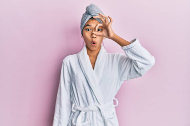 Duş havlusu şapkası ve bornoz giyen genç Çinli kadın şaşırmış yüz ifadesiyle şaşırmış ve parmaklarından içeri bakıyordu. İnançsız ifade. 