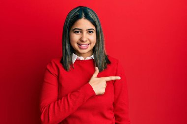 Yüzünde mutlu ve doğal bir ifade olan, elleri ve parmaklarıyla işaret eden, güler yüzlü, gündelik kıyafetler giyen genç Latin kadın. 