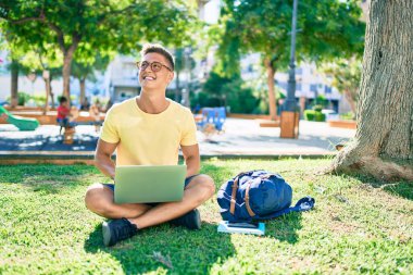 Üniversite kampüsünde çimlerin üzerinde otururken mutlu bir şekilde gülümseyen İspanyol öğrenci.