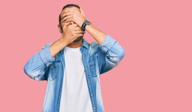 Uzun saçlı, sakallı, sıradan kot ceket giyen, gözlerini ve ağzını elleriyle kapatan çekici bir adam. Şaşırmış ve şok olmuş. duygu gizleme 