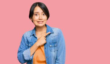 Genç, kısa saçlı, sıradan kot ceketli, endişeli ve gergin bir kadın işaret parmağıyla endişeli ve şaşırmış bir ifade takınıyor. 