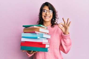 Genç İspanyol kadın elinde bir yığın kitap tutuyor parmaklarıyla imza atıyor, gülümsüyor ve mükemmel bir sembol oluşturuyor. 