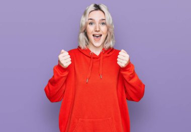 Gündelik giysiler giyen genç sarışın kız şaşkınlık ve şaşkınlık içinde kollarını kaldırarak ve gözlerini açarak başarıyı kutluyor. Kazanan konsept. 