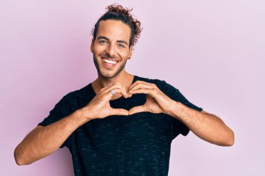 Uzun saçlı, sıradan kıyafetler giyen, aşkla gülümseyen, kalp sembolü ve elleri olan genç, yakışıklı bir adam. romantik kavram. 