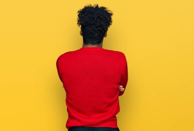 Sakallı, kışlık süveter giyen genç, Afro-Afrikalı Amerikalı bir adam arkasını dönüp kollarını kavuşturmuş bakıyor. 