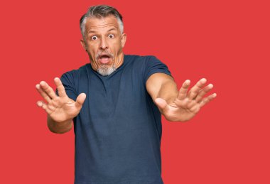 Orta yaşlı, gri saçlı, günlük kıyafetler giyen, korku ifadesinden korkan, dehşete düşmüş, elleri titreyen, şok içinde bağıran bir adam. panik konsepti. 