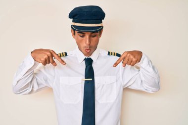 Uçak pilotu üniforması giyen genç İspanyol adam parmaklarını göstererek reklamı gösteriyor, şaşırmış yüz ve ağzı açık. 