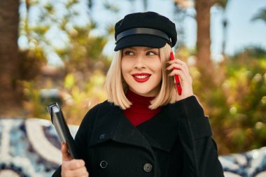 Genç sarışın kadın gülümsüyor. Parktaki akıllı telefondan konuşarak mutlu oluyor..