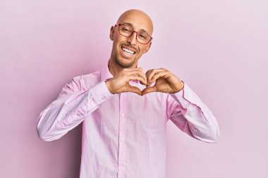 Sıradan kıyafetler ve gözlük takan kel bir adam aşıkken gülümsüyor. Elleriyle kalp sembolü yapıyor. romantik kavram. 