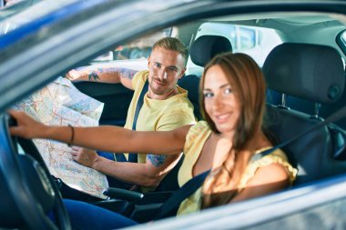 Genç çift gülümsüyor, mutlu araba kullanıyor ve şehir haritasına bakıyor..