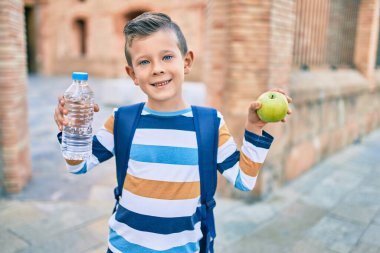 Sevimli beyaz çocuk gülümseyerek yeşil elma ve bir şişe su tutuyor..
