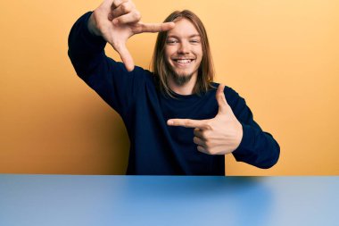 Yakışıklı, beyaz saçlı, günlük kıyafetler giyen, masaya oturmuş gülümseyen, elleri ve parmakları gülen yüzlü bir adam. yaratıcılık ve fotoğrafçılık kavramı. 