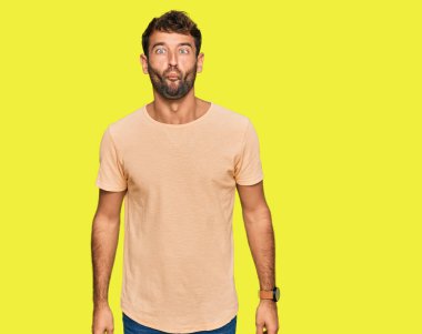 Sakallı, sıradan tişörtlü, dudakları balık suratlı, çılgın ve komik hareketler yapan yakışıklı bir genç. Komik ifade. 