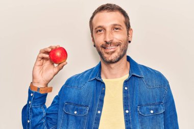 Genç yakışıklı adam kırmızı elma tutuyor. Pozitif ve mutlu görünüyor. Duruyor ve gülümsüyor. 