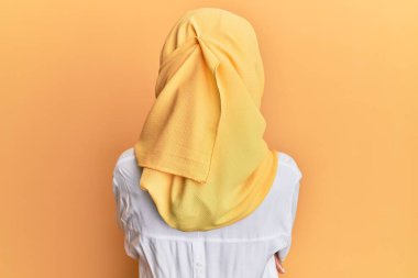 Geleneksel İslami başörtüsü takan genç esmer Arap kadın geriye doğru çapraz kollarla bakıyor. 