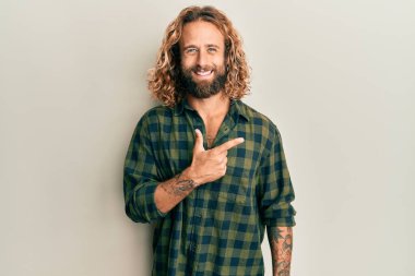 Sakallı, uzun saçlı, günlük kıyafetler giyen, neşeli yüzlü, elleri ve parmaklarıyla yüzünü gösteren, mutlu ve doğal bir ifadeyle yakışıklı bir adam. 