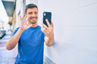 Kafkasyalı genç adam şehirde akıllı telefon kullanarak video araması yaparken mutlu gülümsüyor..