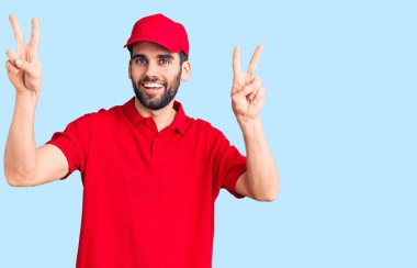 Sakallı, teslimat üniforması giyen, ağzı açık gülümseyen, iki elini de zafer işareti yapan genç yakışıklı bir adam. İki numara.. 