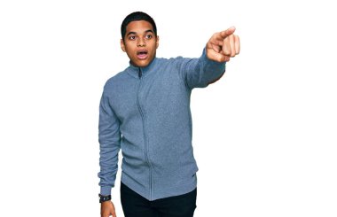 Genç, yakışıklı, sıradan bir kazak giyen, parmağıyla işaret eden, ağzı açık, ağzı açık, şaşırmış, ön tarafta bir şey var. 