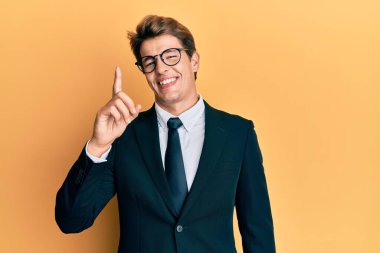 Yakışıklı beyaz adam iş elbisesi ve kravat takıyor. Bir numaralı parmağını gösterip işaret ediyor. Kendine güvenen ve mutlu.. 
