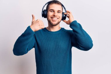 Müzik dinleyen, kulaklık takan, mutlu ve olumlu gülümseyen, başparmağını kaldıran, mükemmel ve onay işareti yapan genç yakışıklı bir adam. 