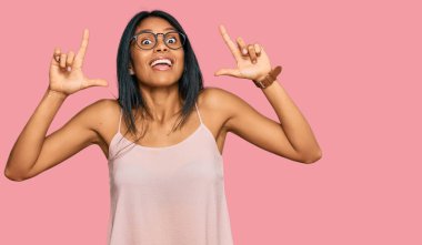 Genç Afrikalı Amerikalı kadın günlük kıyafetler ve gözlük takıyor. Şaşırmış, şaşırmış ve parmaklarıyla işaret ediyor ve kollarını kaldırıyor.. 