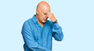 Orta yaşlı, kel, günlük kıyafetler giyen, burnu ve gözleri ovuşturmaktan yorgun, yorgunluk ve baş ağrısı çeken bir adam. Stres ve hüsran kavramı. 