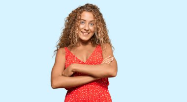 Yazlık elbise giyen güzel beyaz kız kollarını kavuşturup kameraya bakarken gülümsüyor. pozitif kişi. 