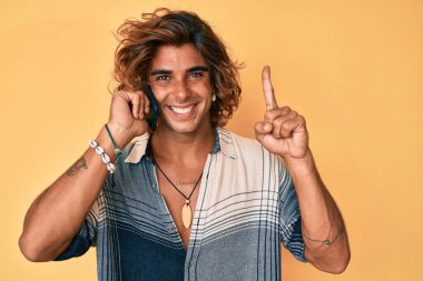 Genç İspanyol bir adam akıllı telefondan konuşuyor. Bir fikir veya soruyla gülümsüyor. Mutlu bir yüzle işaret ediyor. 