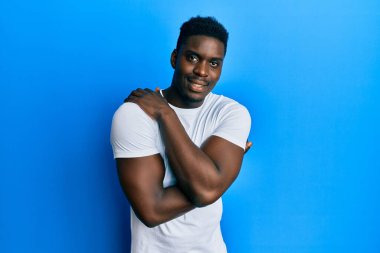 Yakışıklı, beyaz tişört giyen, kendine sarılan, mutlu ve pozitif, kendinden emin gülümseyen bir zenci. Sevgi ve özgüven. 