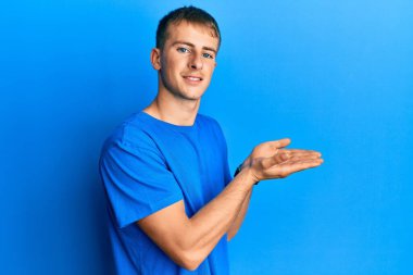 Sıradan mavi tişört giyen genç beyaz adam avuçlarını açıp fotokopi alanını gösteriyor. Gülümseyen mutlu bir gülümseme. 