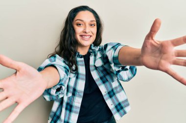 Güzel bir ortadoğulu kadın, günlük giysiler içinde kameraya bakıyor ve sarılmak için kollarını açmış gülümsüyor. Mutluluğu kucaklayan neşeli bir ifade.. 