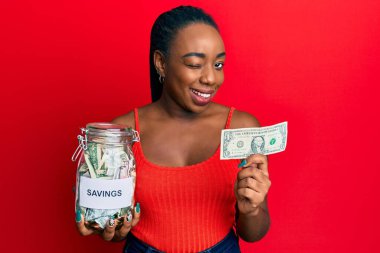 Genç Afrikalı Amerikalı kadın elinde bir kavanoz birikimle kameraya seksi bir ifadeyle bakıyor, neşeli ve mutlu bir yüzle.. 