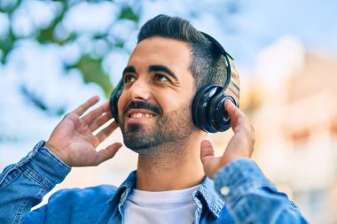 Şehirde kulaklık takarak mutlu gülümseyen genç İspanyol adam..