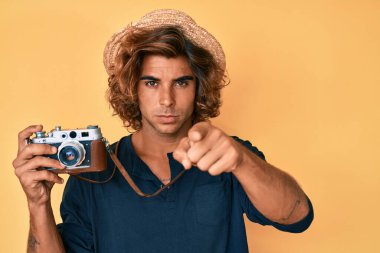 Şapkalı genç İspanyol bir adam kamerayı işaret eden klasik bir kamera tutuyor ve sen kendine güvenen ciddi bir hareket yapıyorsun. 